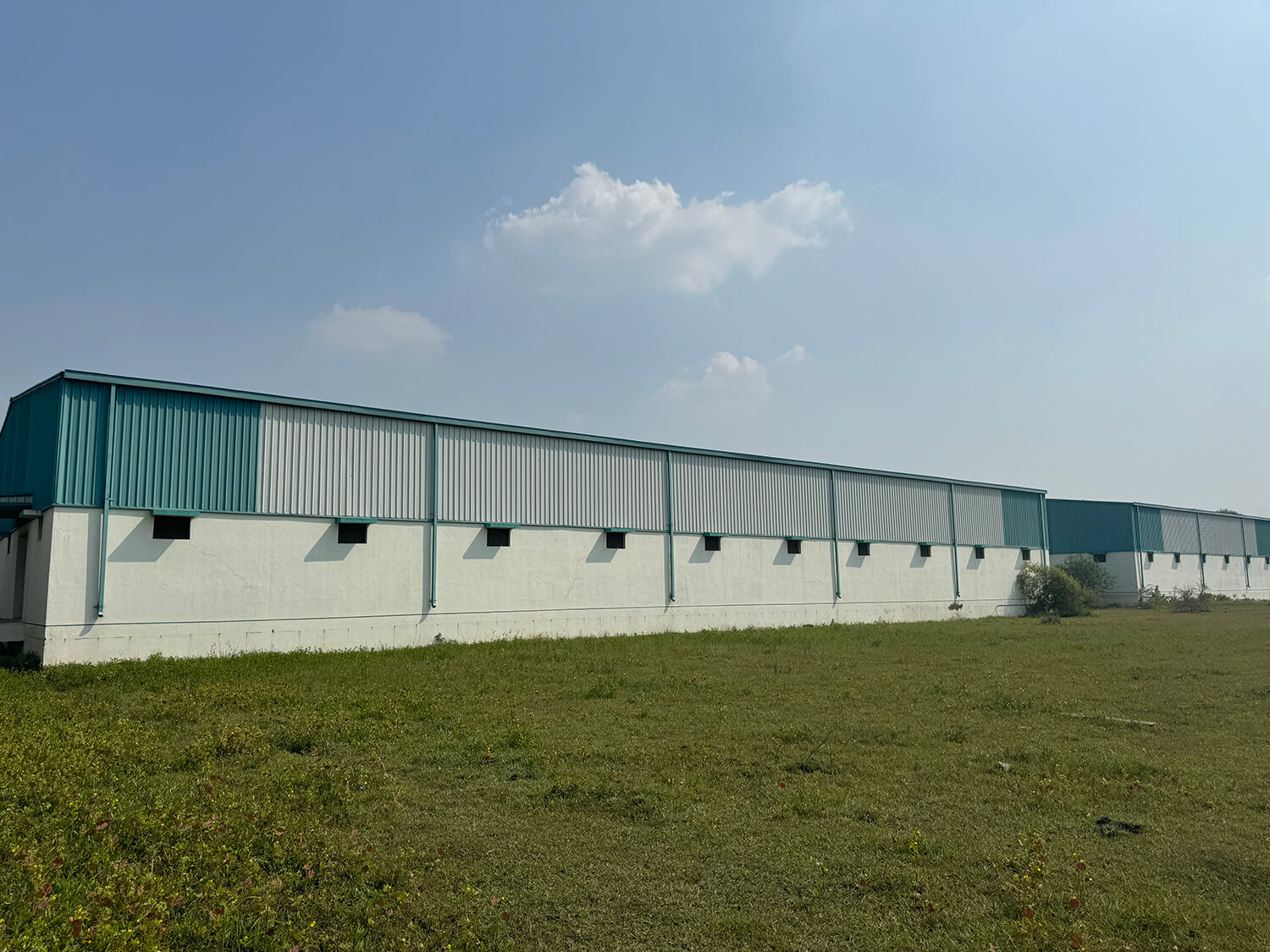 Metal warehouse building with a grassy field in front.